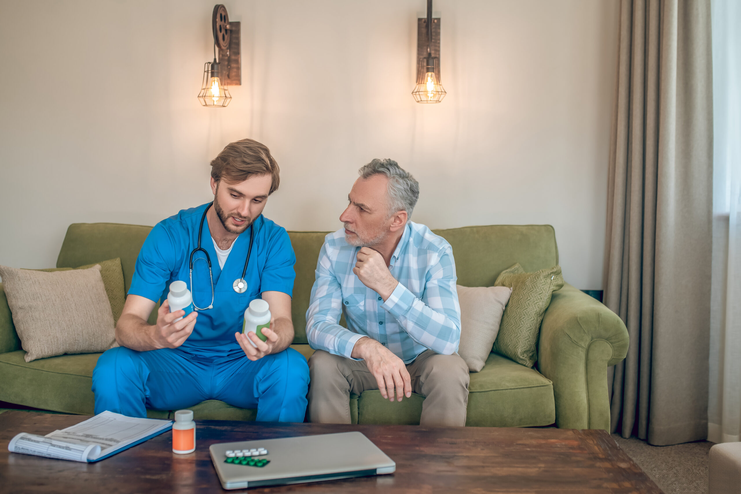 Front view of a young doctor with plastic vitamin bottles in his hands talking to a mature man