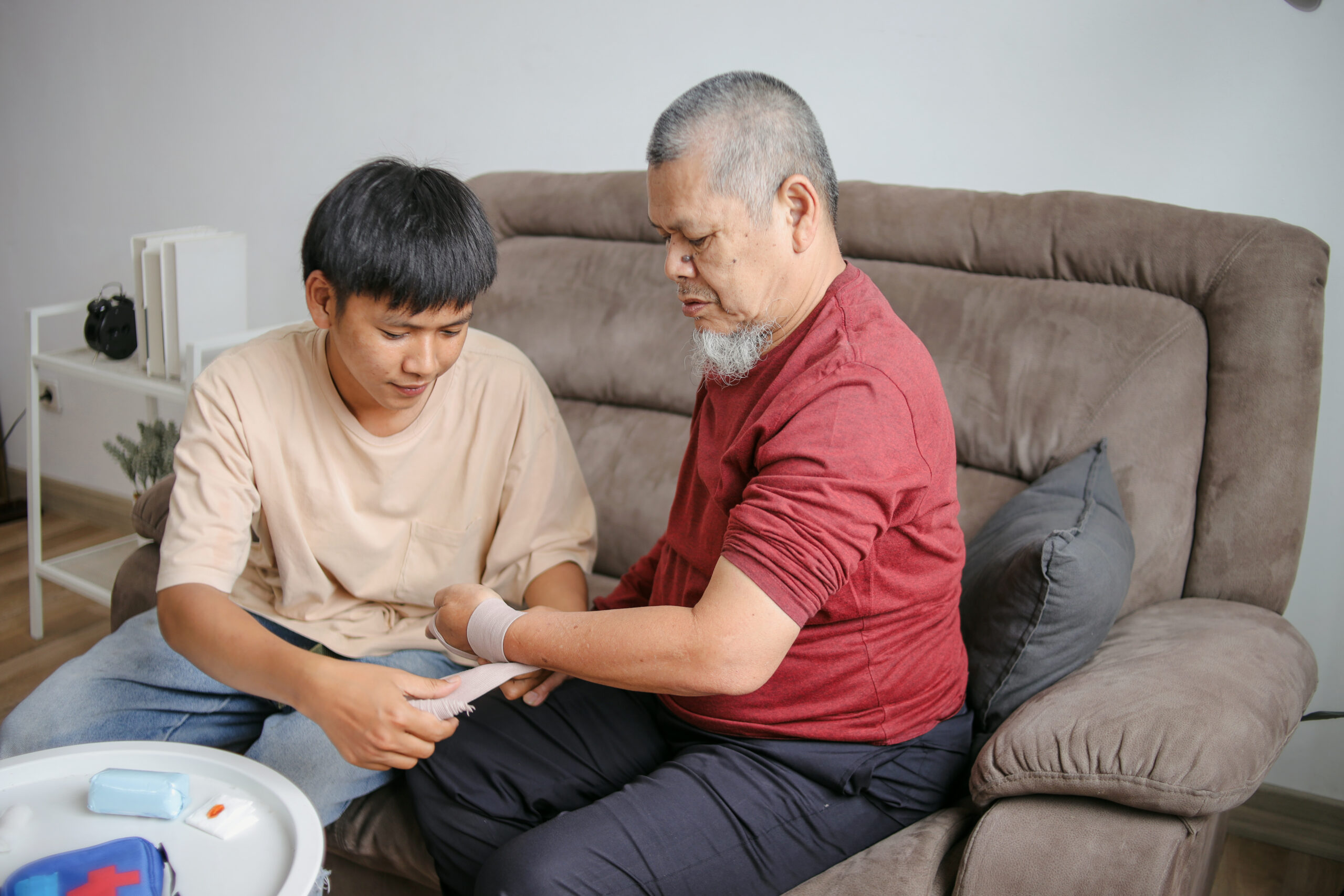 Young Asian Man Wrapping Grandfather's Injured Hand Sprained Wrist With Bandage