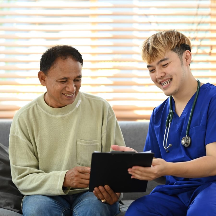 Young male doctor sharing good health test news with happy senior man during home visiting. Medical insurance, elderly medical health care concept.