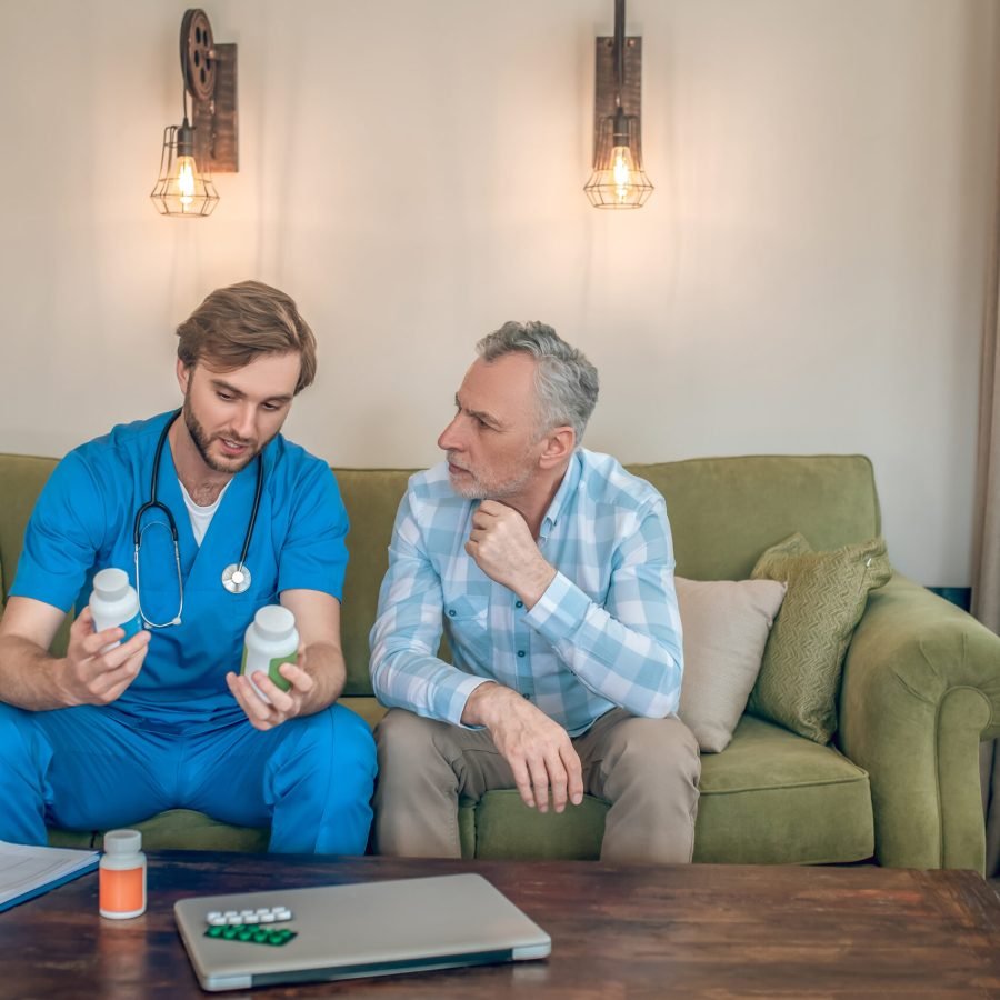Front view of a young doctor with plastic vitamin bottles in his hands talking to a mature man