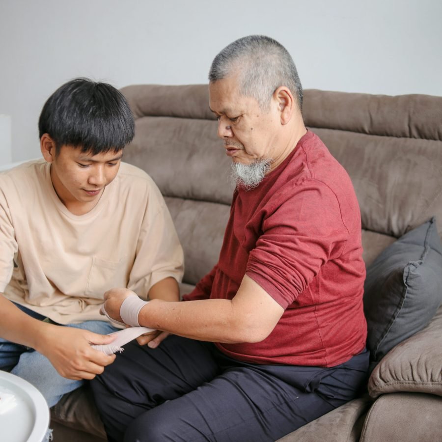 Young Asian Man Wrapping Grandfather's Injured Hand Sprained Wrist With Bandage